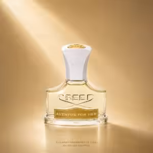 Creed Aventus For Her profumo donna, flacone trasparente con dettagli dorati in packshot luxury su sfondo dorato.